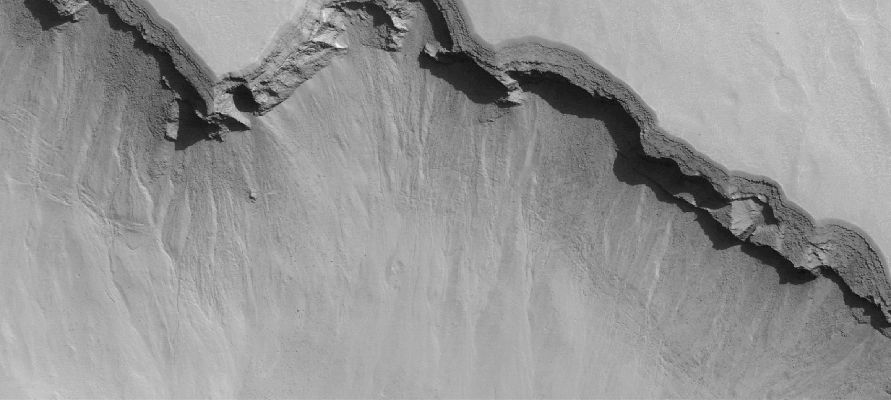 Features of Noachis Terra (Original NASA/MGS/MSSS b/w Frame)
Caption NASA Originale:"This MGS-MOC image shows the edge of a trough, which is part of a large pit crater complex in Noachis Terra. This type of trough forms through the collapse of surface materials into the subsurface and often begins as a series of individual pit craters. Over time, continued collapse increases the diameter of individual pits until finally, adjacent pits merge to form a trough such as the one captured in this image. The deep shadowed area is caused in part by an overhang; layered rock beneath this overhang is less resistant to erosion, and thus has retreated tens of meters backward, beneath the overhang. A person could walk up inside this "cave" formed by the overhanging layered material".

Location near: 47,0° South; 355,7° West
Image width: ~3 Km (~1,9 mi)  
Illumination from: upper left  
Season: Southern Summer
Parole chiave: Mars from orbit - Troughs