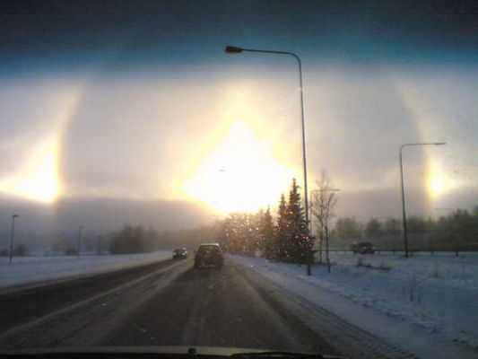 Suomi's Sundogs
What's happened to the Sun? Sometimes it looks like the Sun is being viewed through a large lens. In the above case, however, there are actually millions of lenses: ice crystals. As water freezes in the upper atmosphere, small, flat, six-sided, ice crystals might be formed. As these crystals flutter to the ground, much time is spent with their faces flat, parallel to the ground. An observer may pass through the same plane as many of the falling ice crystals near sunrise or sunset. During this alignment, each crystal can act like a miniature lens, refracting sunlight into our view and creating phenomena like parhelia, the technical term for sundogs. The above image was taken during early 2006 February near Helsinki, Finland with a quickly deployed cellular camera phone. Visible in the image center is the Sun, while two bright sundogs glow prominently from both the left and the right. Also visible is the 22° halo also created by sunlight reflecting off of atmospheric ice crystals. 
Parole chiave: Amatorial Pictures