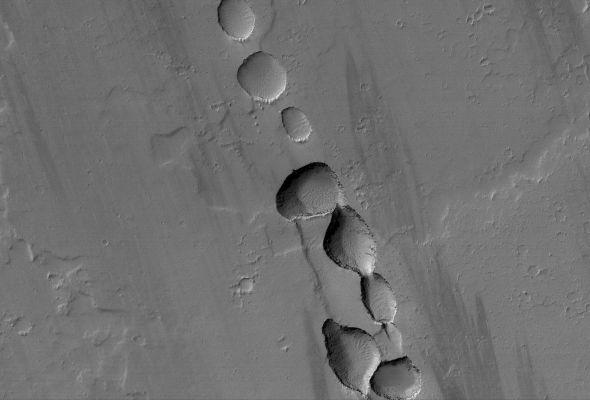 Collapse Pit-Chain near Tharsis Tholus (Original NASA/MGS/MSSS b/w Frame)
Caption NASA originale:"This MGS-MOC mage shows a portion of a Chain of Collapse Pits on a Lava and Dust-covered Plain, North/West of Tharsis Tholus —one of the many volcanic constructs in the Tharsis Region of Mars. 
Pit chains, such as this one, are associated with the collapse of surface materials into subsurface voids formed by faulting and expansion — or extension — of the bedrock".

Location near: 16,4° North Lat. and 92,6° West Long.
Image width: ~3 Km (~1,9 mi)  
Illumination from: lower left  
Season: Northern Winter
Parole chiave: Mars from orbit - Volcanic Features - Pit Chain